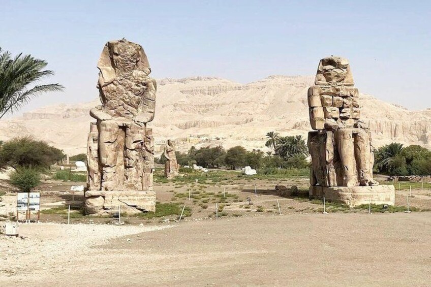 Two large stone statues in a desert landscape with mountains in the background. 3
