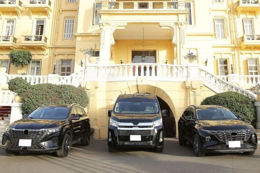 Three black SUVs parked in front of a yellow building with a white balcony and a white fence. 3