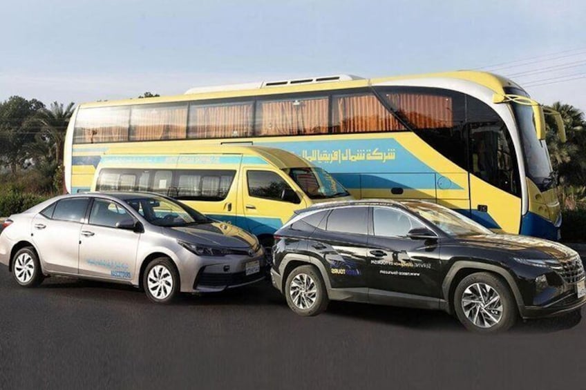 A yellow and blue bus with Arabic text, two cars parked in front, and a clear sky. 2