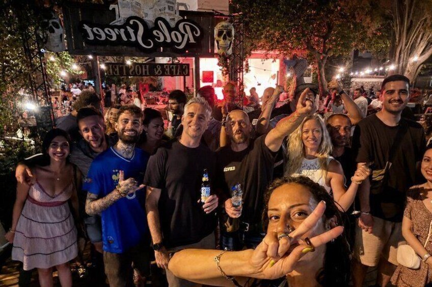 A group of people at a nighttime outdoor event with a sign that reads 'Tale of the City.' 1