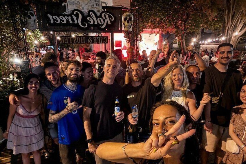 A group of people gathered at a nighttime outdoor event with a sign that reads 'Tee Room.' 1