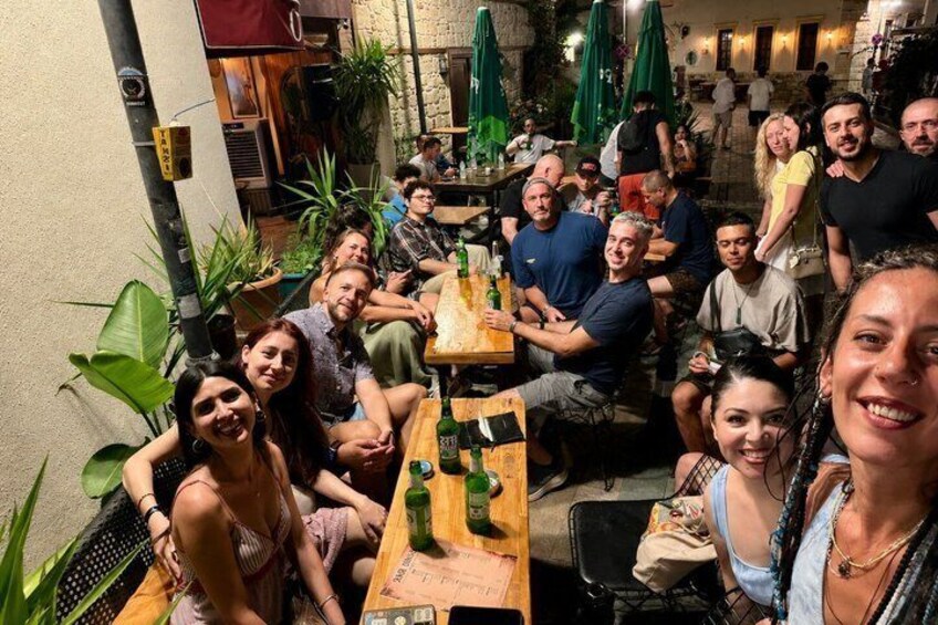 A group of people gathered around tables in an outdoor setting with plants and umbrellas. 3
