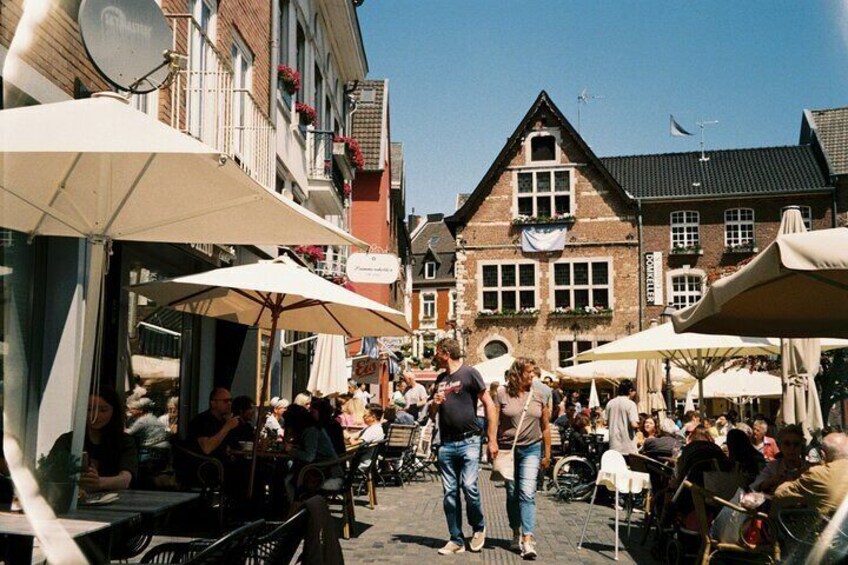 A bustling outdoor café with patrons seated under umbrellas, surrounded by historic buildings. 2