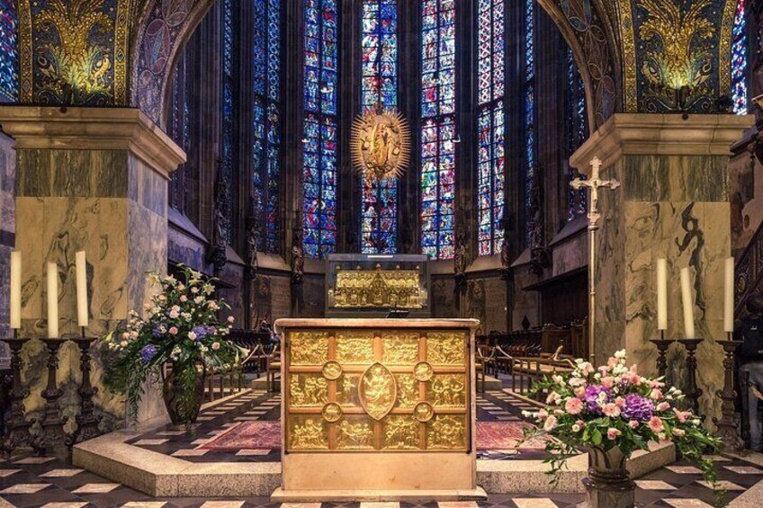 A church interior with a golden altar, stained glass windows, and floral arrangements. 5
