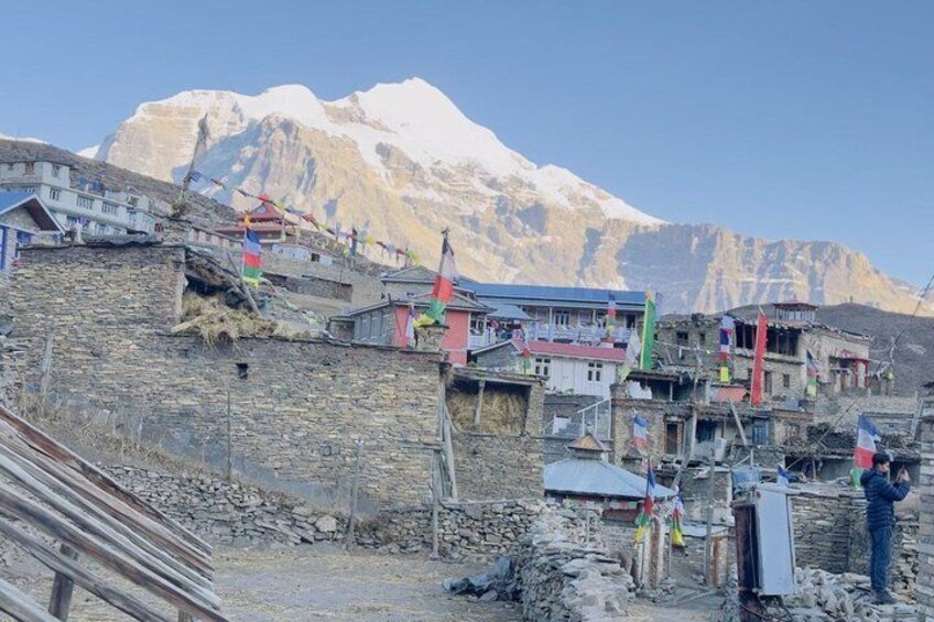 A mountainous village with stone houses, flags, and a snow-capped peak in the background. 1