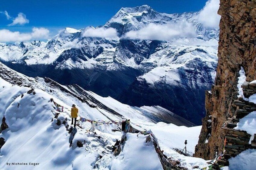 A snowy mountain landscape with a person in a yellow jacket standing on a rocky outcrop. 4