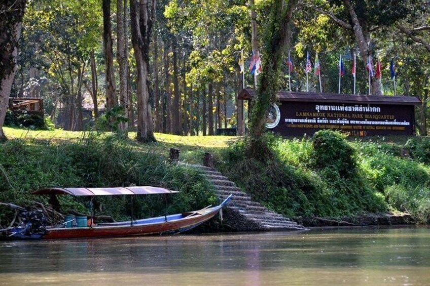 A river with a boat docked, surrounded by lush greenery and a signboard. 4