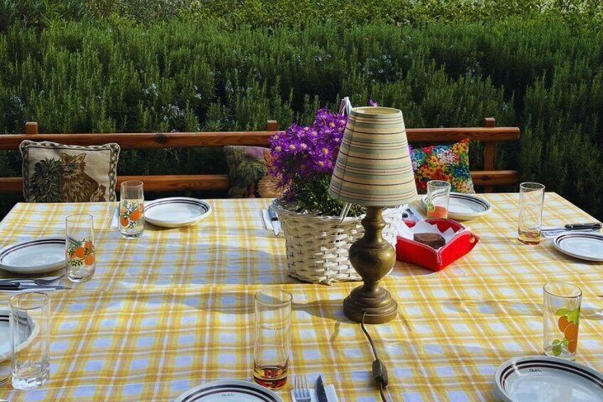 A table set outdoors with a checkered tablecloth, plates, glasses, a lamp, and a basket with flowers. 4