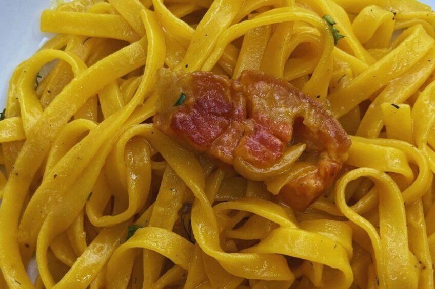 A plate of yellow pasta with a piece of bacon. 5