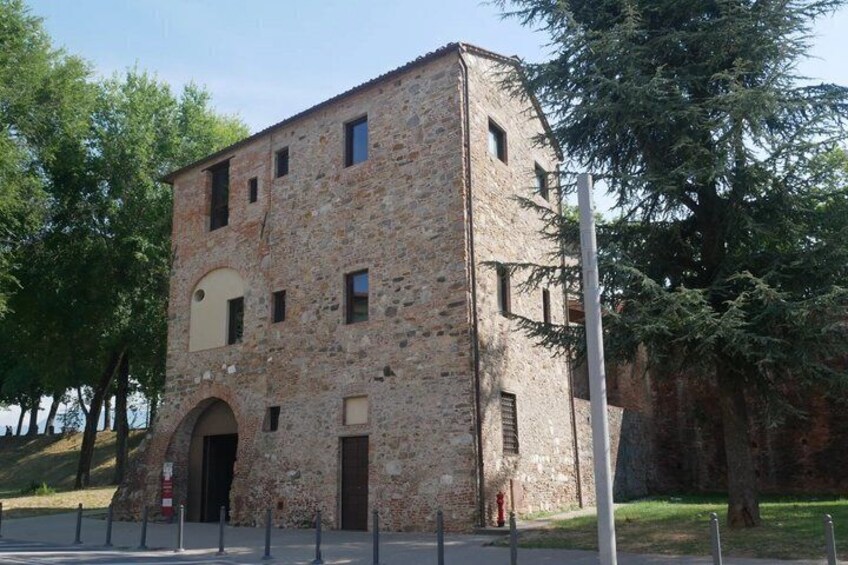 A stone building with a central arched entrance, surrounded by trees and a grassy area. 2