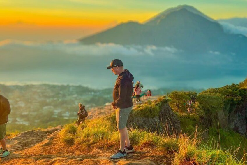 A person standing on a grassy hill overlooking a mountainous landscape with a sunset in the background. 5