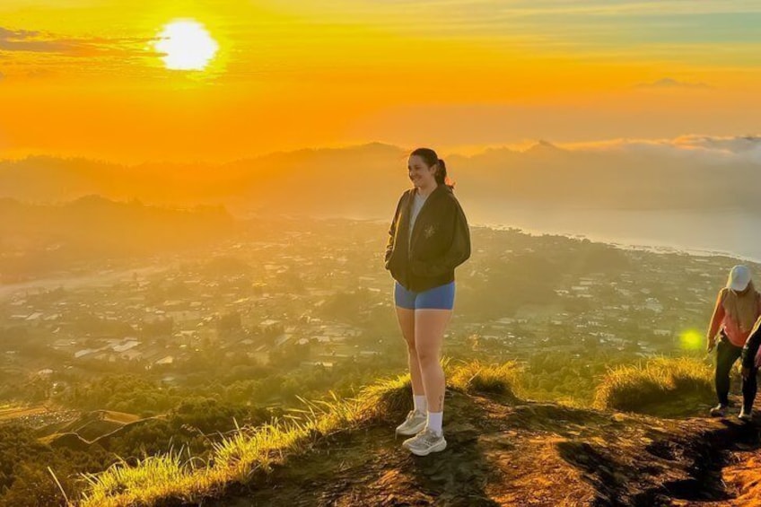 A person standing on a grassy hill overlooking a valley during sunset. 1