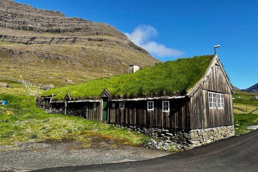 A row of wooden houses with grass roofs, set against a mountainous backdrop. 2
