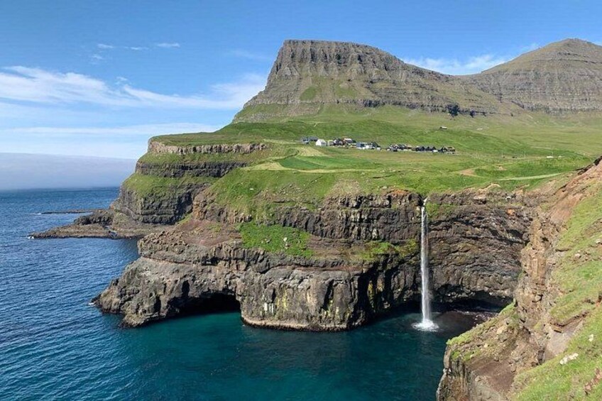 A coastal landscape with a waterfall, cliffs, and a distant mountain. 5