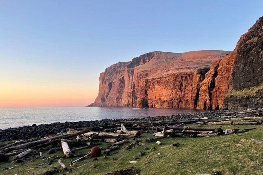 A coastal landscape with cliffs, a rocky beach, and a calm sea. 2