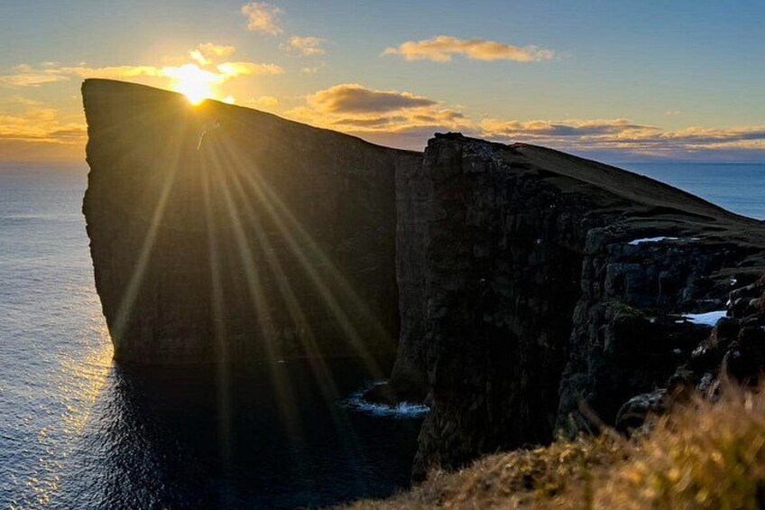 A large rock formation with the sun setting behind it, casting rays of light. 4