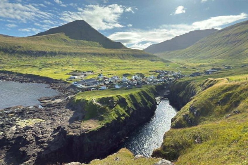 A coastal village with houses, a narrow water channel, and green hills. 1