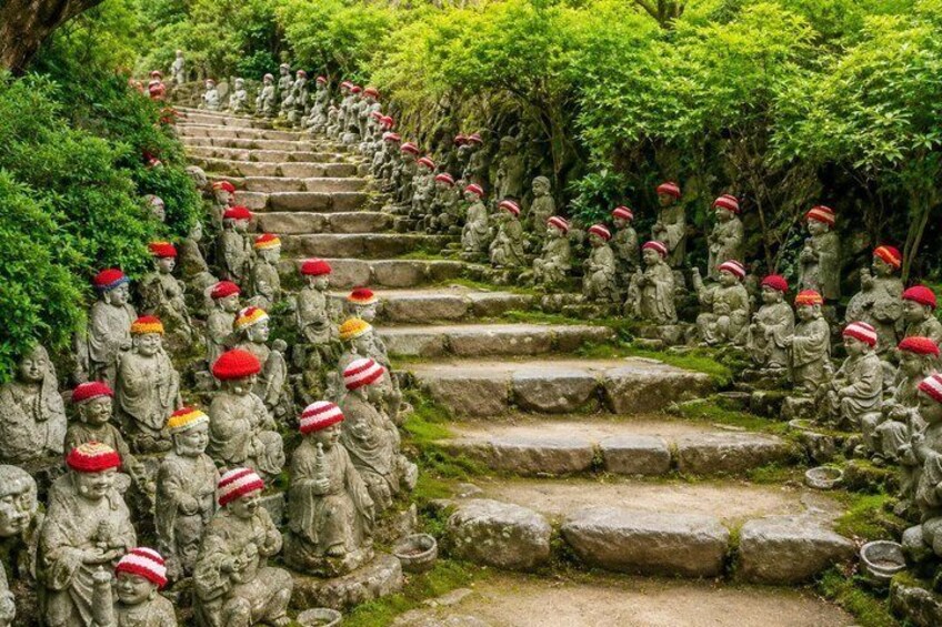 A stone staircase with numerous statues of figures wearing red hats, surrounded by lush greenery. 4