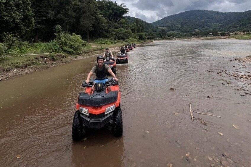 People riding ATVs on a muddy riverbank. 1