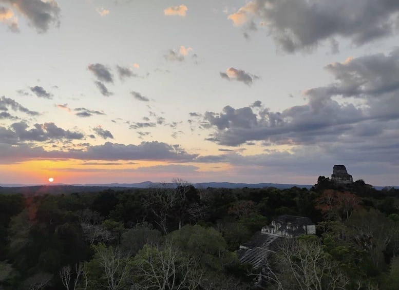 A sunset over a landscape with a pyramid-like structure and dense foliage. 1