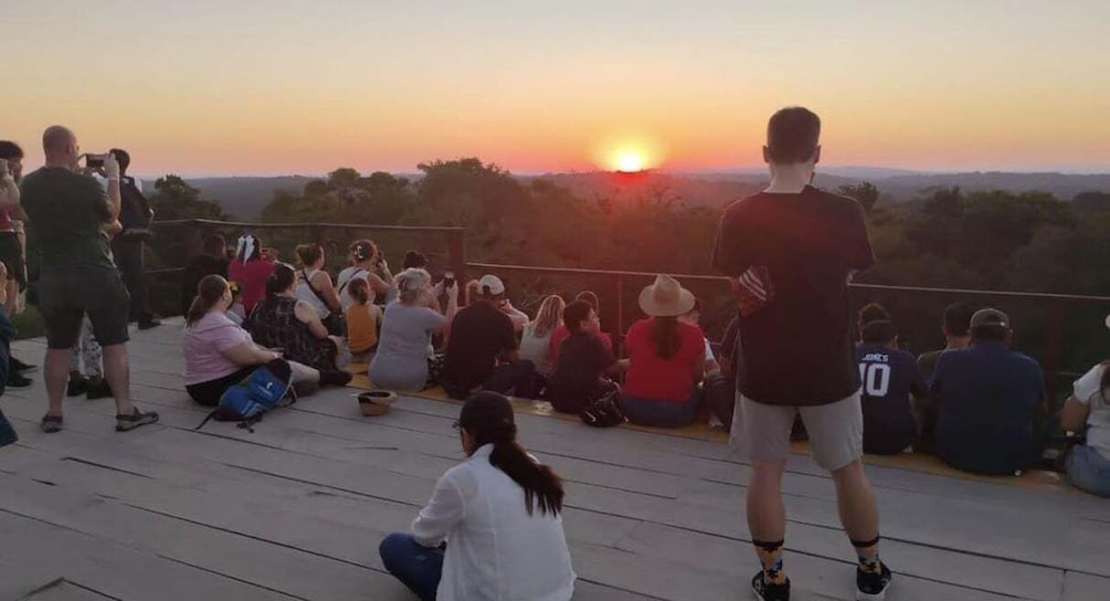 A sunset over a crowd of people on a wooden deck. 1