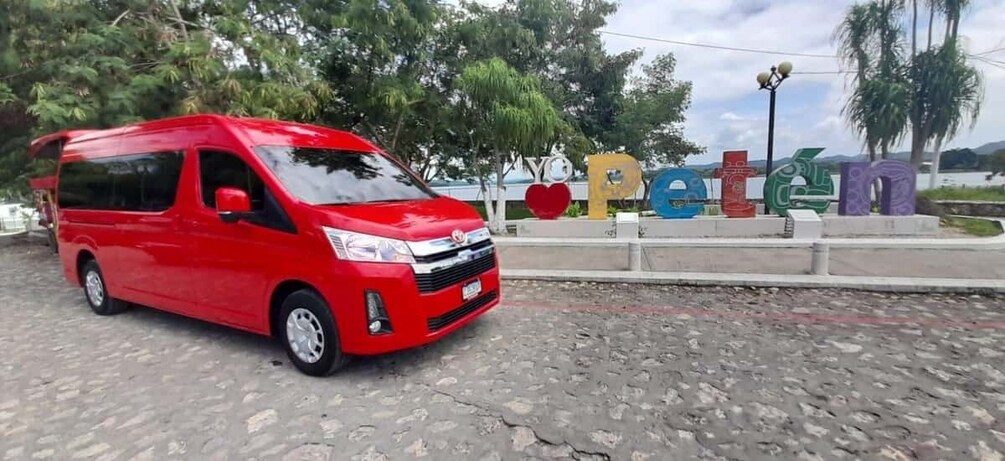 A red van parked on a cobblestone street with colorful letters spelling 'Petén' in the background. 5