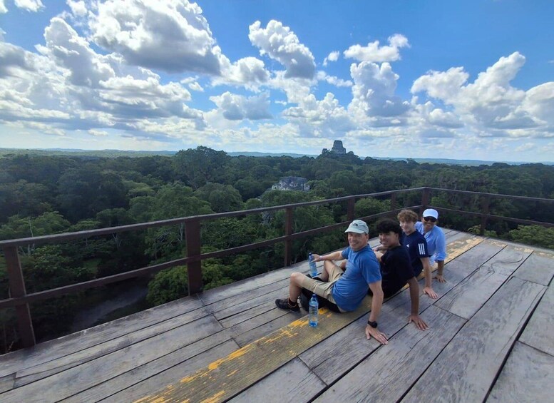 A group of people on a wooden observation deck overlooking a forested landscape with a distant hill. 2