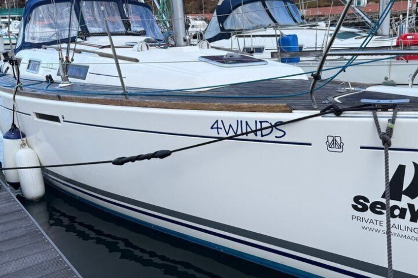 A white boat named '4 WINDS' docked at a marina with other boats and a blue buoy. 4