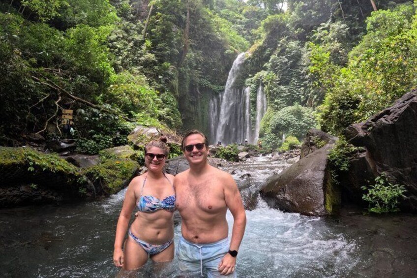 A couple standing in a forested area with a waterfall in the background. 4