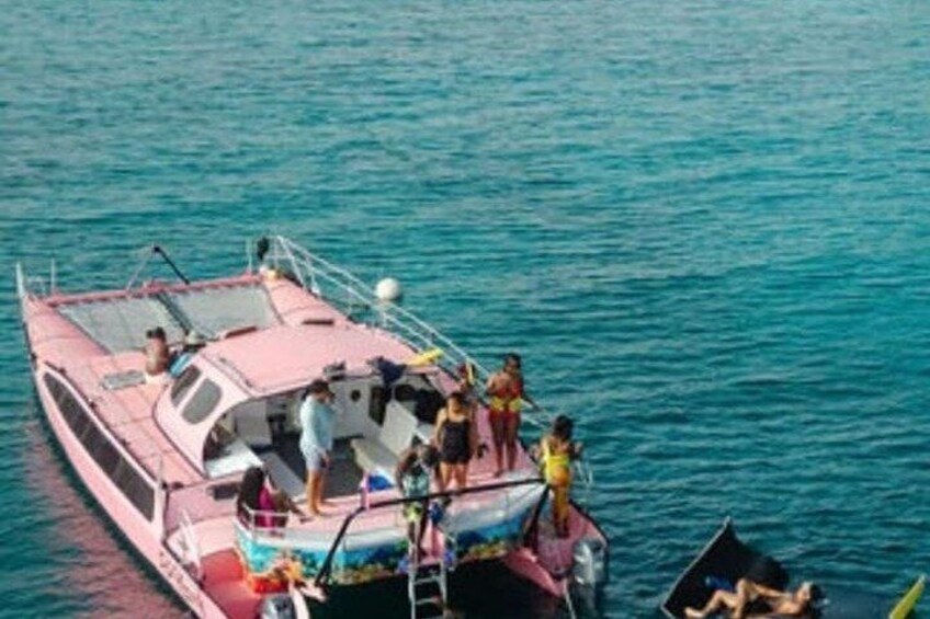 A boat with people standing on the deck, some in the water, and a smaller boat nearby. 1