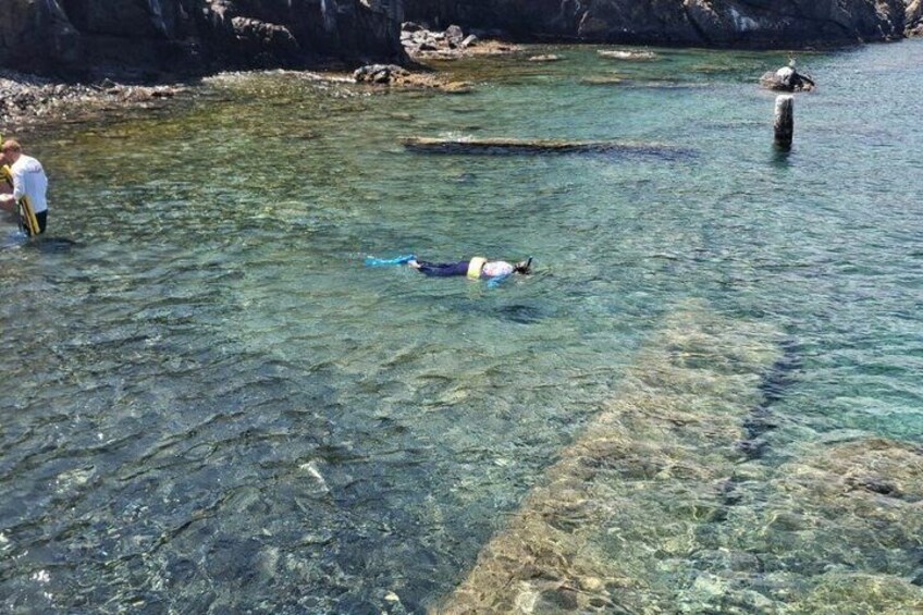 A person swimming in clear water near rocks. 2