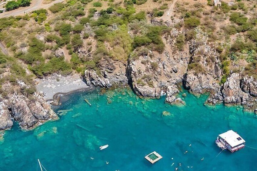 A coastal landscape with rocky cliffs, clear turquoise waters, and a boat anchored near the shore. 3