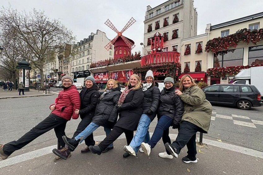 A group of people posing in a city street with a windmill and a building with a sign that reads 'Hôtel de Ville.' 2