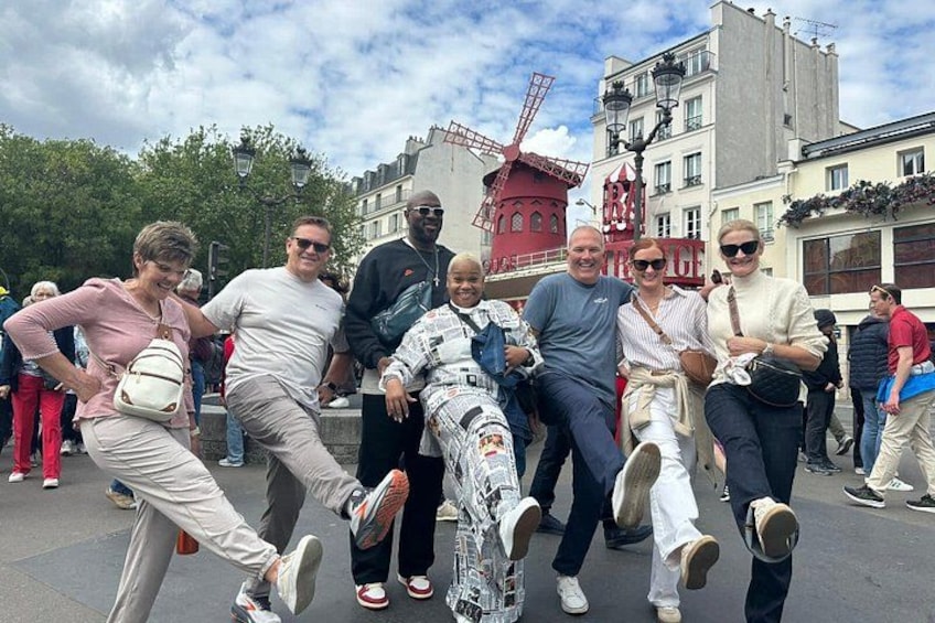 A group of people posing in front of a windmill and buildings. 3