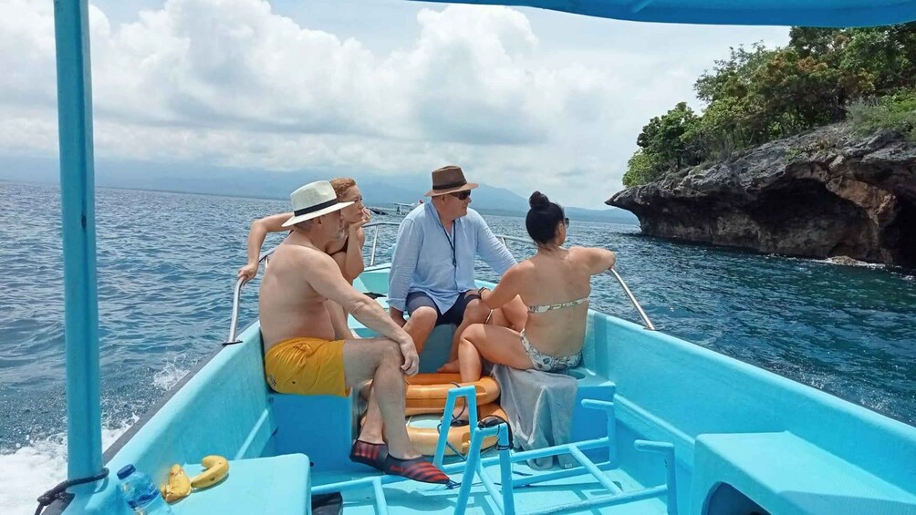 A group of people on a blue boat with a rocky coastline in the background. 2