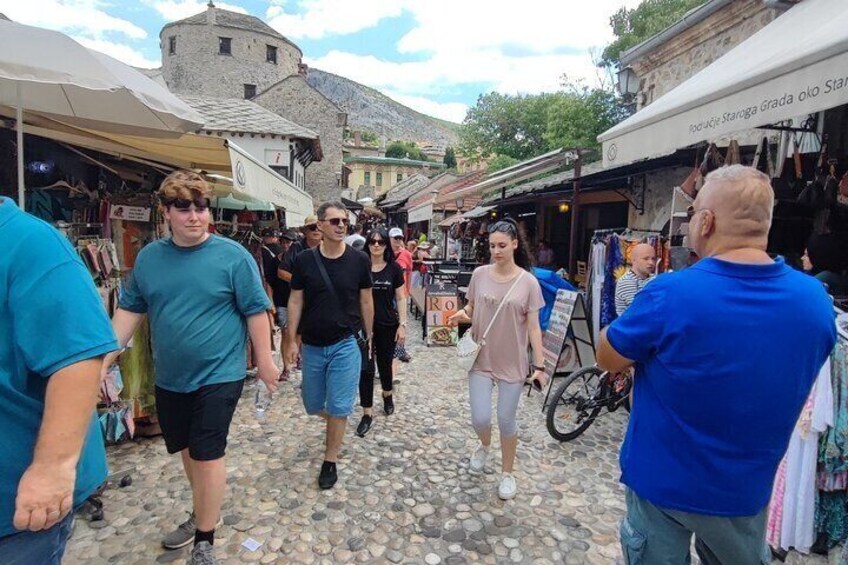 A cobblestone street with people walking, market stalls, and a historic building in the background. 4