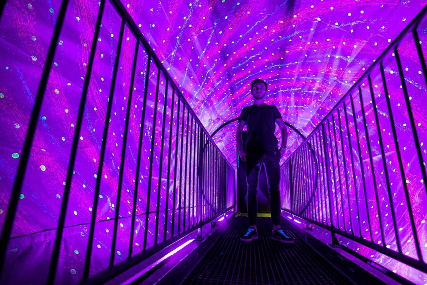 A person standing in a tunnel with purple lighting and metal railings. 2