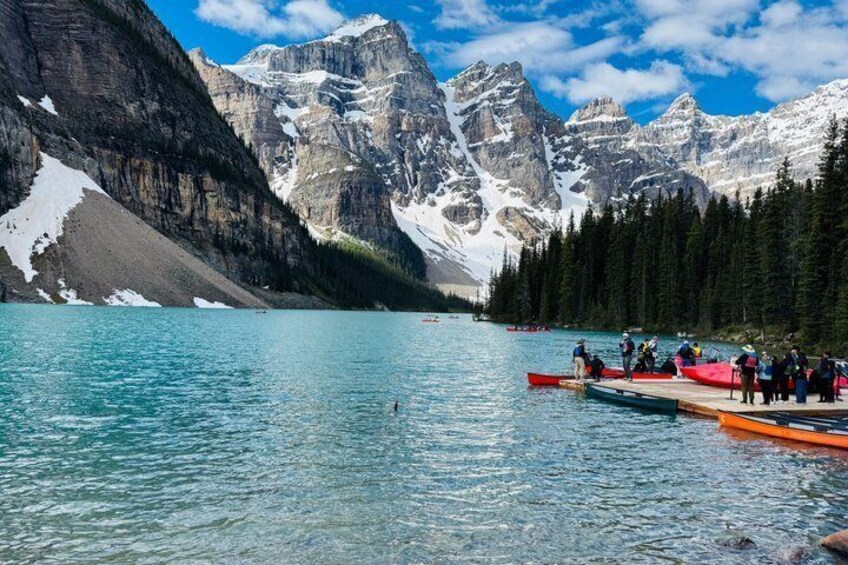 A calm lake with boats, surrounded by snow-capped mountains and dense forest. 5