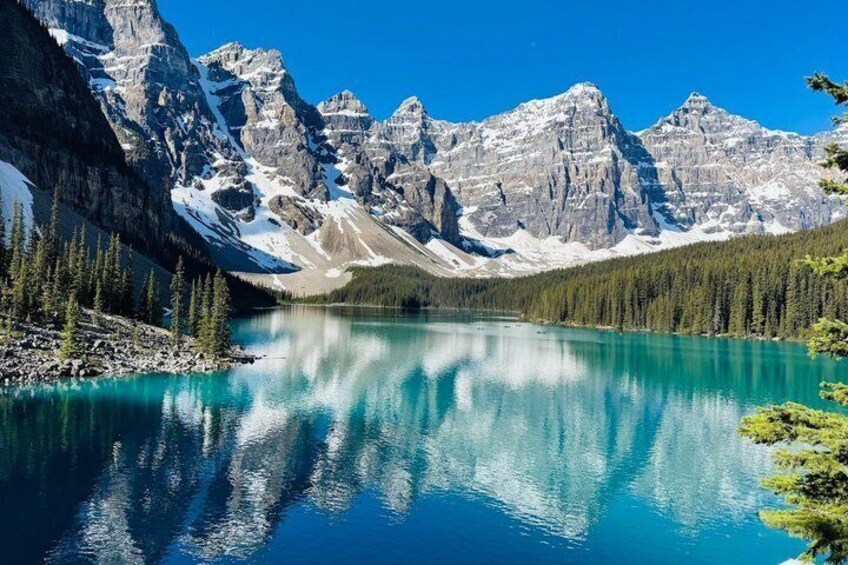 A mountain lake with clear turquoise water, surrounded by snow-capped peaks and dense forest. 4
