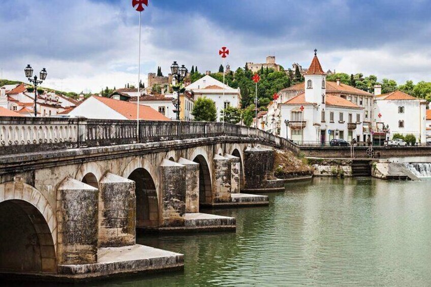 A stone bridge over a river with buildings and a tower in the background. 1