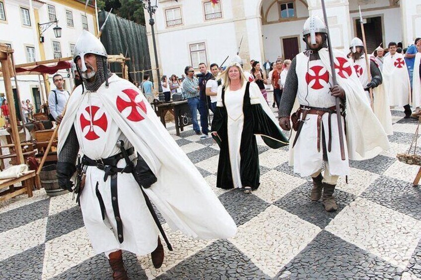 People in medieval costumes with white and red symbols, walking on a cobblestone street. 2