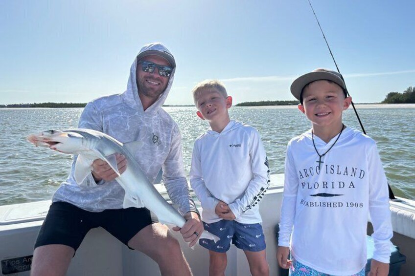 Three people on a boat holding a fish, with water and a distant shoreline in the background. 3