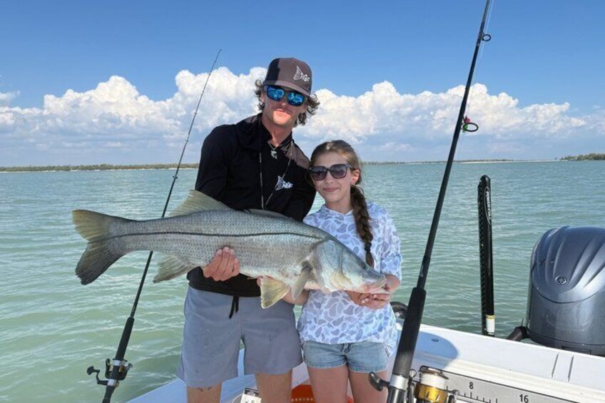 Two people holding a large fish on a boat with fishing rods in the background. 1