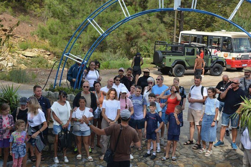 A group of people gathered around a blue arch structure, with a green and white bus in the background. 2
