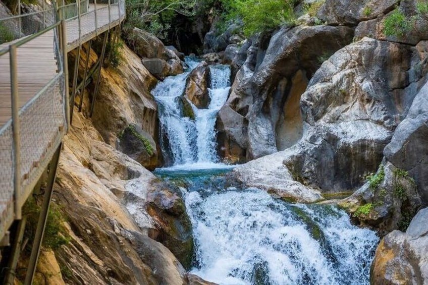 A waterfall cascading over rocks, a wooden bridge, and lush greenery. 1