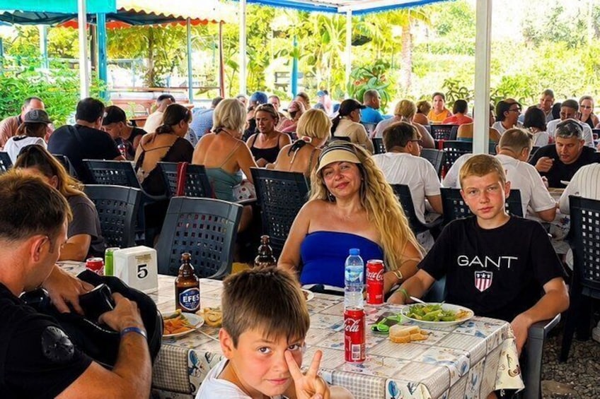 A group of people dining outdoors at a covered area with tables and chairs. 5