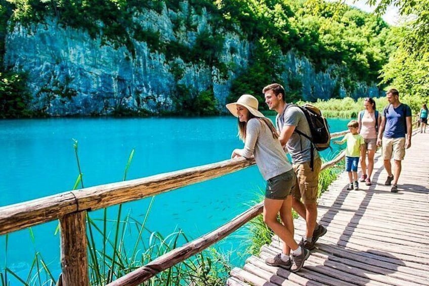 A wooden boardwalk by a turquoise lake with rocky cliffs. 1