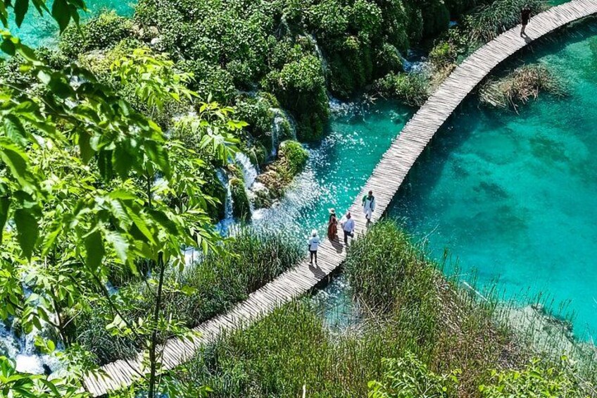A wooden bridge over a turquoise river, surrounded by lush greenery and a waterfall. 4