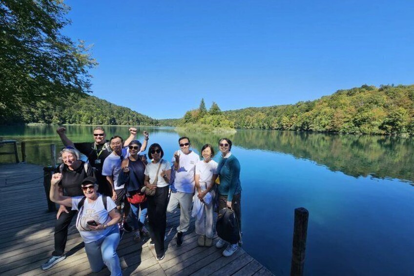 A group of people on a wooden dock by a calm lake surrounded by trees. 2