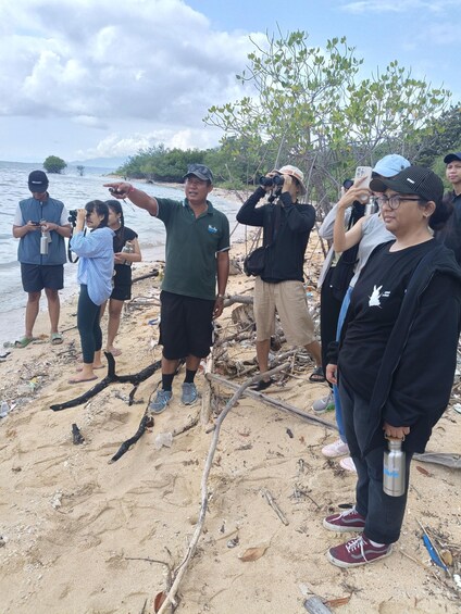 A group of people on a sandy beach with a tree and a body of water in the background. 5